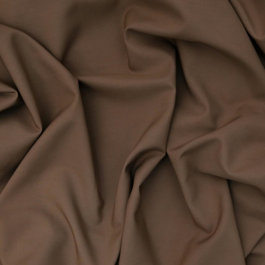 Close-up of soft brown fabric with elegant draped folds, shot indoors.
